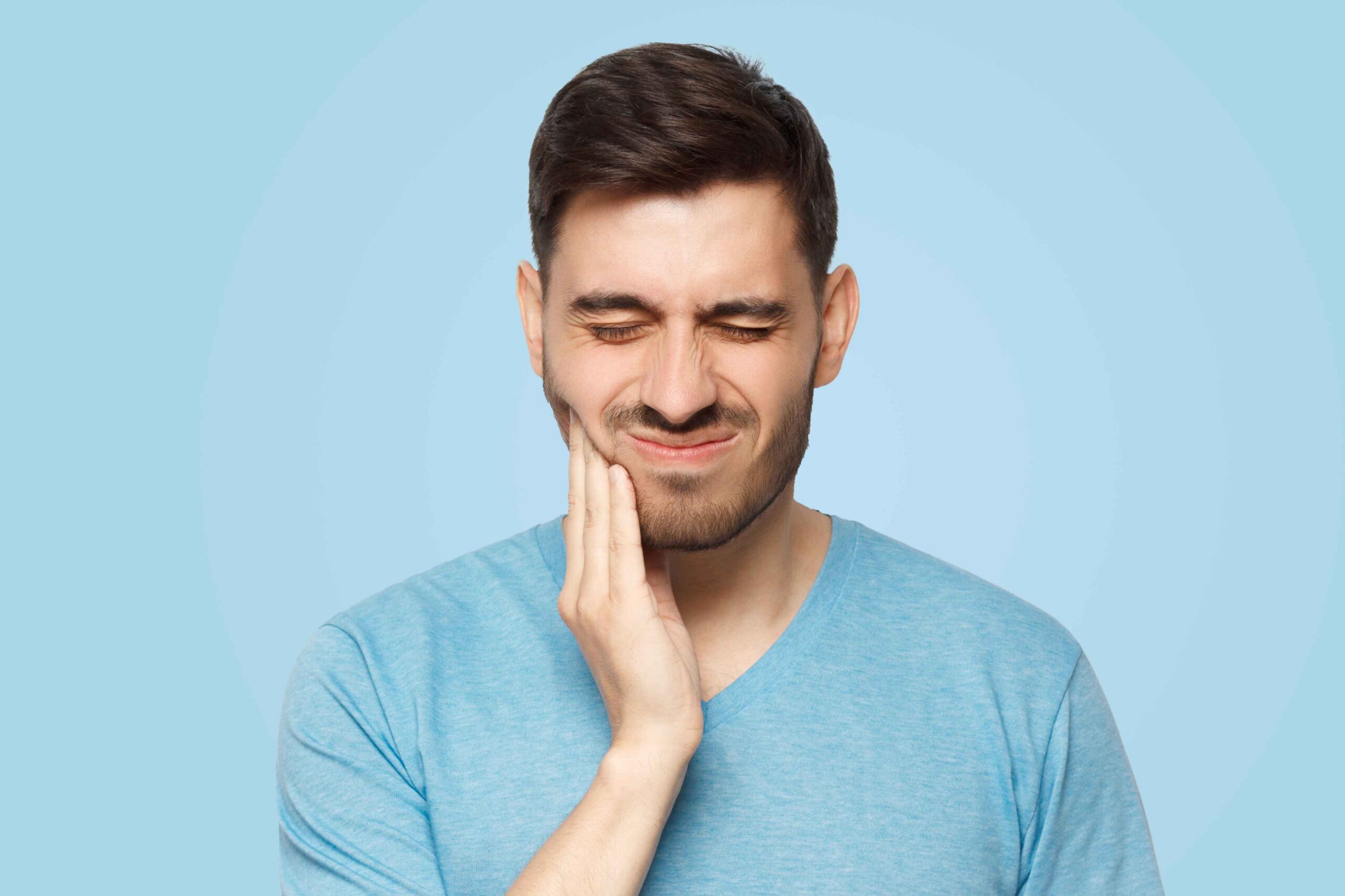 Man holding his cheek while experiencing tooth pain.